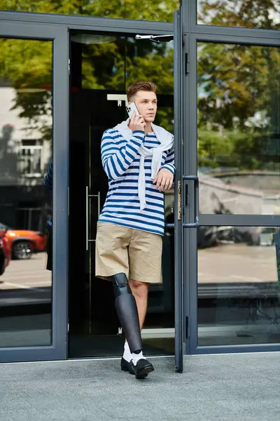 A stylish young man stands at the entrance, chatting on his phone while embracing life. — Stock Photo