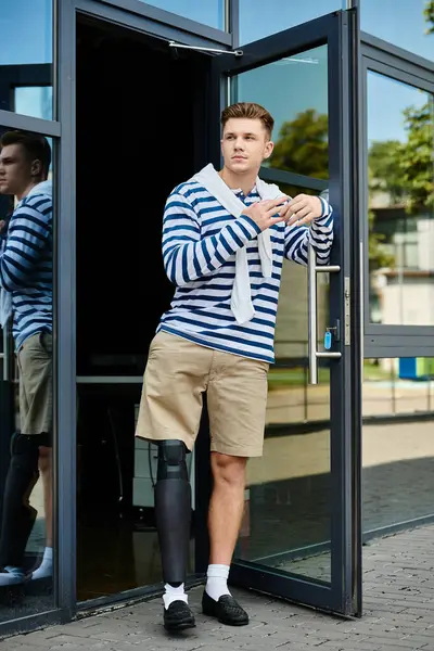 A young man leans against the doorway, proudly displaying his prosthetic leg. — Stock Photo