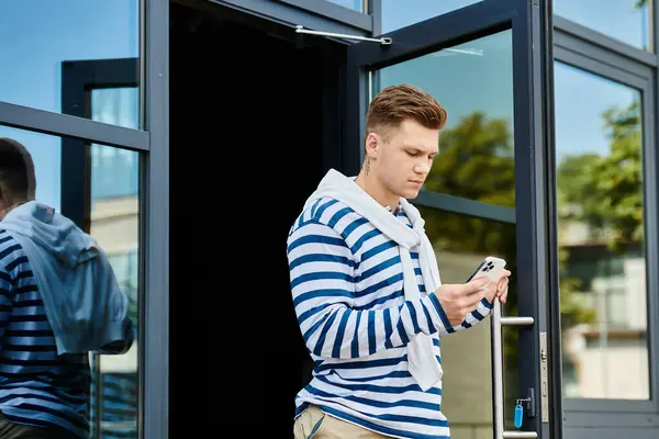 A young man wearing a striped sweater stands near the entrance, focused on his phone. — Stock Photo