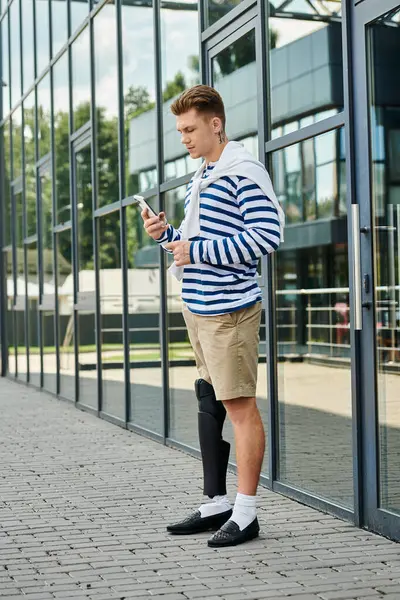 Un joven guapo con una pierna protésica se para con su smartphone al aire libre. — Stock Photo