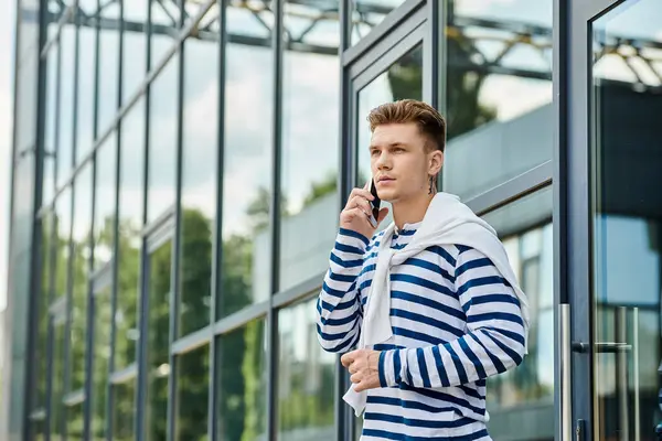 A young man stands confidently outside, conversing on his mobile phone in casual style. — Stock Photo