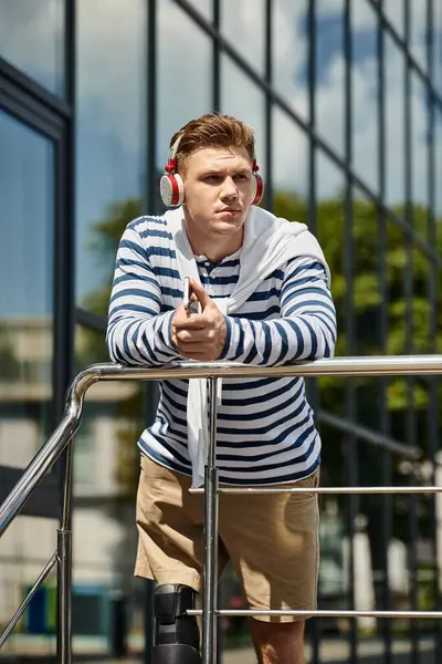 The young man leans against a railing, immersed in music while enjoying the warm sun. — Photo de stock