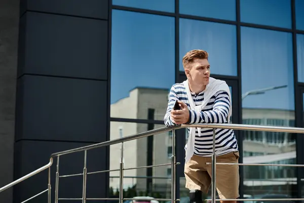 A young, handsome man with a prosthetic leg leans against a railing, focused on his phone. — Stock Photo