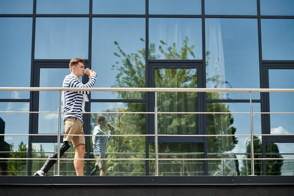 A young man confidently strolls by, savoring a drink and embracing the outdoors. — Stock Photo
