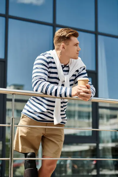 A stylish young man pauses to sip coffee, contemplating life against a vibrant urban backdrop. — Stock Photo