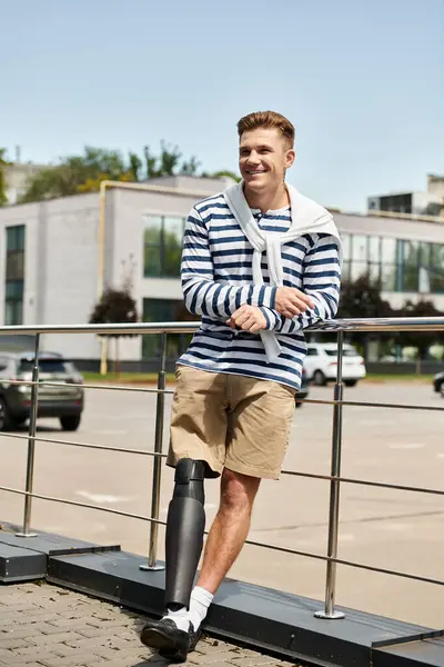 A cheerful young man stands by a railing, showcasing his prosthetic leg while smiling in sunlight. — Stock Photo