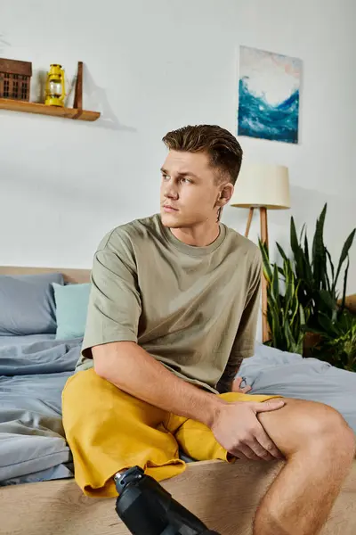 A young man sits on a bed, showing strength and confidence with his prosthetic leg. — Stock Photo