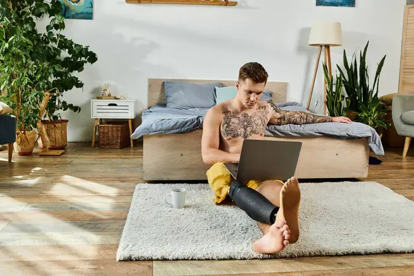 A young man works on his laptop, comfortably seated on a soft rug, showing resilience. — Stock Photo
