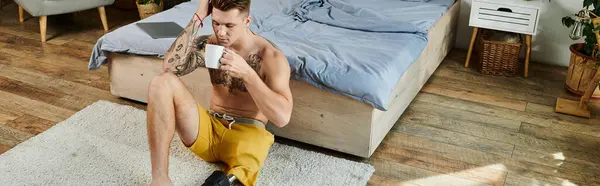 Ein junger Mann sitzt mit Beinprothese auf dem Boden und nippt an einem Kaffee in einem ruhigen Schlafzimmer. — Stockfoto