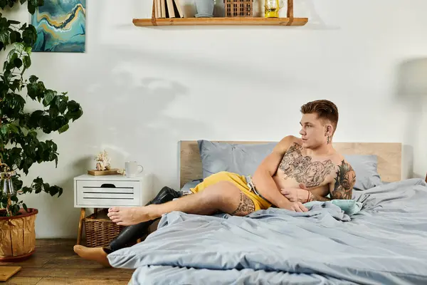 A young man relaxes on a bed, showcasing his prosthetic leg and deep tattoos in a peaceful setting. — Stock Photo