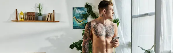 The young man stands thoughtfully by the window, showcasing his tattoos and prosthetic leg. — Stock Photo