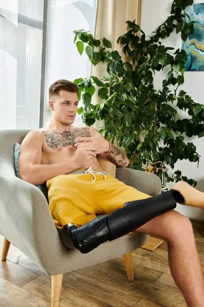 Um jovem bonito senta-se confortavelmente em uma cadeira, mostrando sua perna protética enquanto relaxado. — Fotografia de Stock
