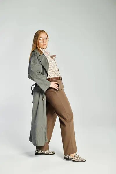 A graceful woman with long hair poses confidently in autumnal outerwear against a subtle grey background. — Stock Photo