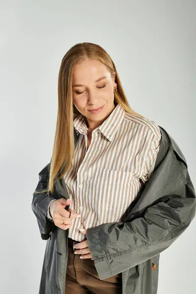 Una donna sofisticata che indossa capispalla autunnale posa con grazia su uno sfondo grigio morbido. — Foto stock