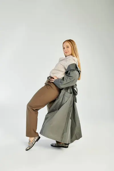 Una donna alla moda mette in mostra il suo ensemble autunnale mentre posa giocosamente in un'atmosfera moderna da studio. — Foto stock