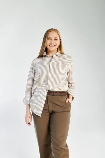 This confident woman with long hair stands in a stylish striped shirt and chic pants, smiling warmly. — Stock Photo