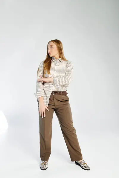 A woman with long hair stands poised in a striped shirt and pants, radiating confidence in a studio. — Stock Photo