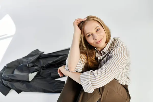 A lovely woman with flowing hair sits gracefully in a studio, showcasing her stylish attire against a grey backdrop. — Stock Photo