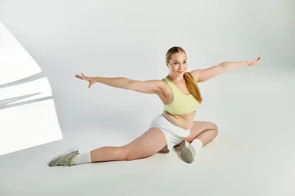 A sporty woman performs a graceful split in a bright studio, showcasing her strength and flexibility. — Stock Photo