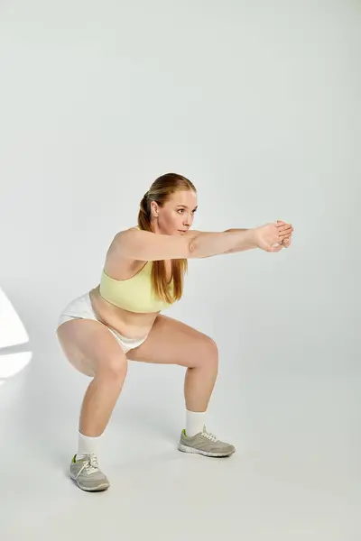 Eine Frau macht selbstbewusst Kniebeugen und präsentiert ihre Fitness-Routine in einem lebendigen Studio-Ambiente. — Stockfoto