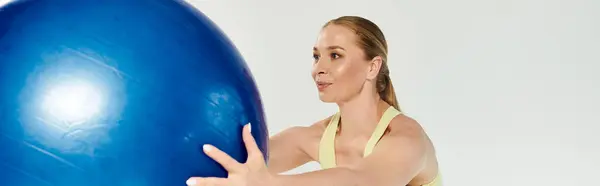 A young woman engages in an energetic workout using a large stability ball in a sunny exercise studio. — Stock Photo