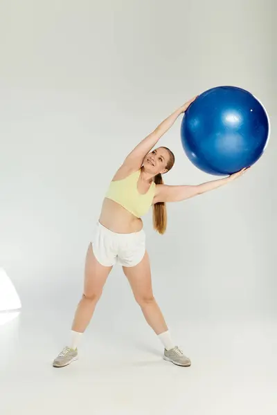 A dynamic athlete wearing a crop top stretches gracefully, incorporating a blue exercise ball in her routine. — Stock Photo