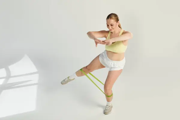 A confident woman in a crop top performs exercises with resistance bands in a bright studio. — Stock Photo