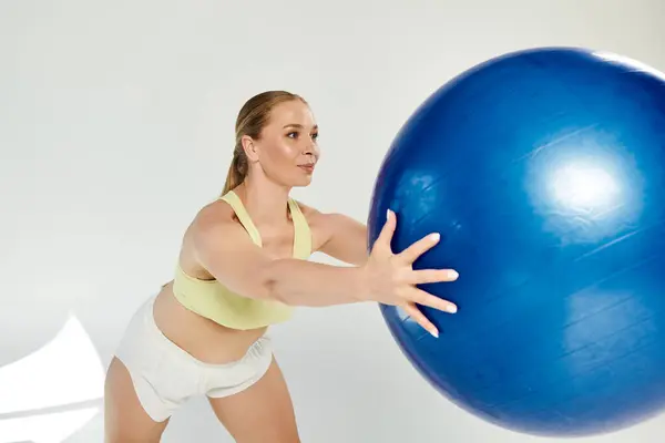 A dedicated sportswoman showcases her strength while exercising with a large blue ball in a studio setting. — Stock Photo