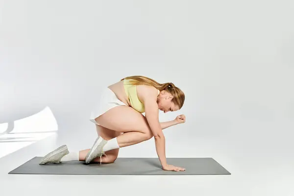 A strong and focused woman performs an energetic exercise on a yoga mat in a welcoming studio space. — Stock Photo