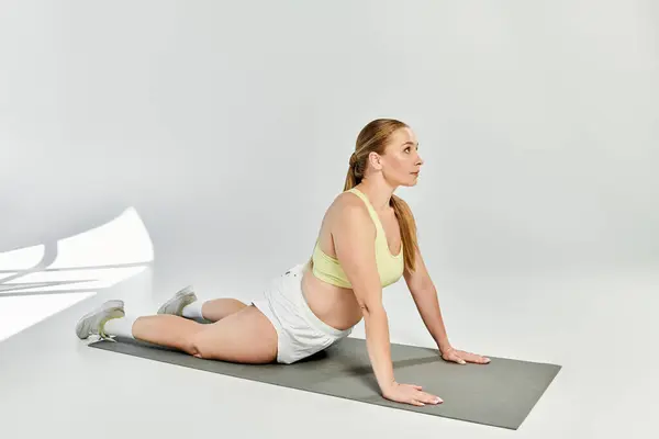 A determined woman in a crop top performs a yoga pose on a mat, embodying strength and focus. — Stock Photo