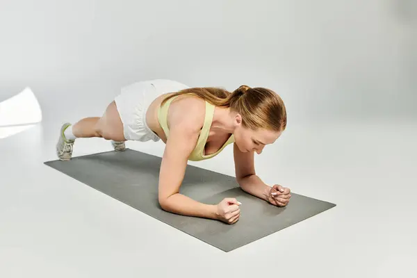 A determined woman exercises in a crop top, mastering the plank position on a mat in a studio. — Stock Photo