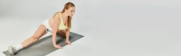 A dedicated woman performs a stretch in a bright studio, focusing on her fitness routine with determination. — Stock Photo