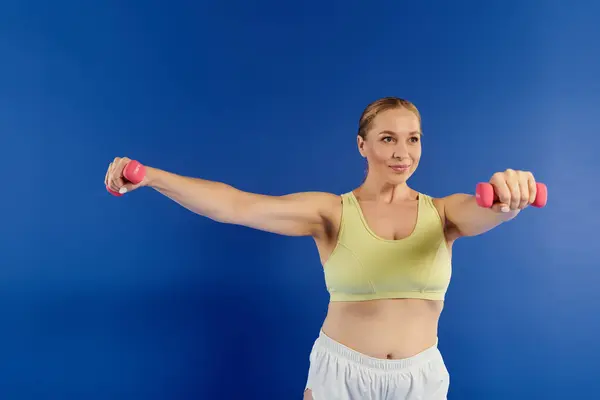 A dedicated woman engages in a dynamic workout, lifting weights confidently in a bright and energetic studio. — Stock Photo