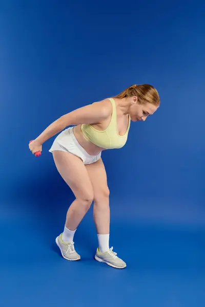 An athletic woman focuses intently while exercising with weights in a bright, colorful studio environment. — Stock Photo