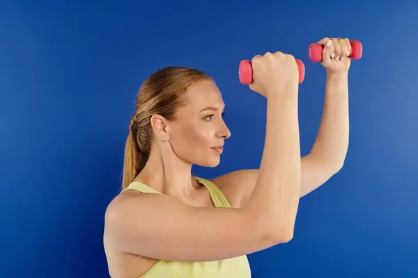 A dedicated woman exercises energetically with bright dumbbells, showcasing strength in a vibrant studio. — Stock Photo