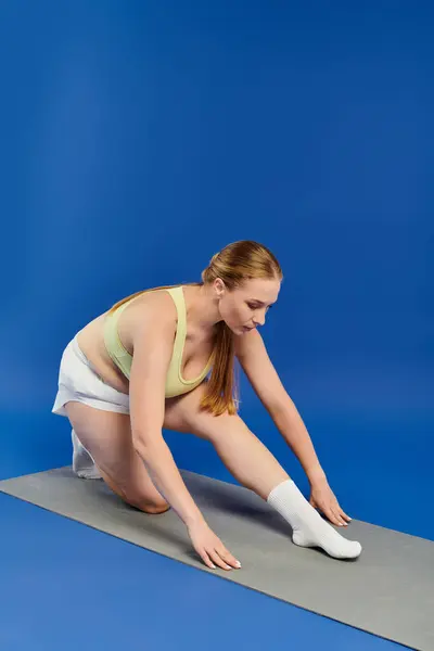 A dedicated sportswoman stretches her legs on a mat in a vibrant studio, showcasing her fitness journey. — Stock Photo