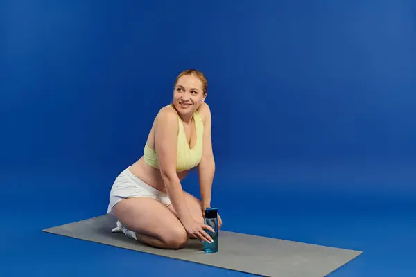 A cheerful woman in a crop top kneels on a mat, engaged in her workout routine within a bright studio. — Stock Photo