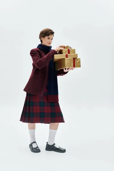 A woman in cozy layers elegantly balances festive gifts in a calm setting. — Stock Photo