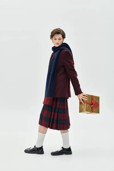 A beautiful woman dressed in cozy winter clothing is holding a wrapped gift, exuding warmth. — Stock Photo