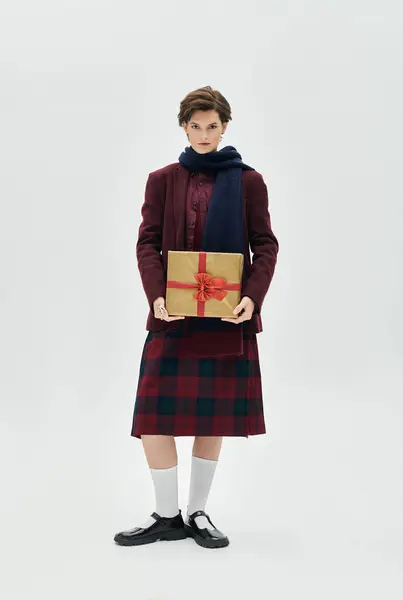 A beautiful woman dressed in elegant winter attire presents a wrapped gift with a bow. — Stock Photo
