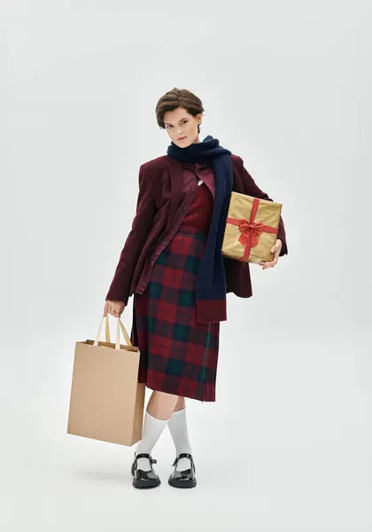 Une femme à la mode affiche son style d'hiver tout en tenant des sacs à provisions et un cadeau. — Photo de stock