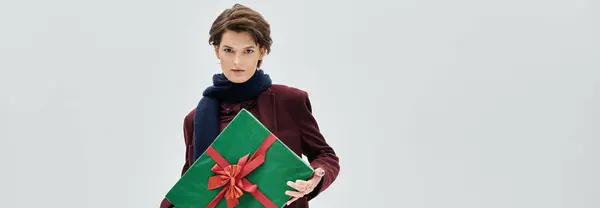 A stunning woman showcases her winter style while presenting a festive green gift with a red bow. — Stock Photo