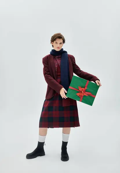 A young woman showcases her cozy winter outfit while presenting a festive gift with grace. — Stock Photo