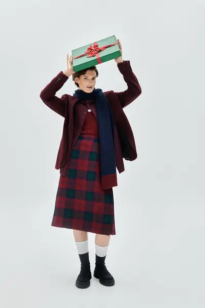 A cheerful woman in elegant winter wear joyfully holds a holiday gift above her head. — Stock Photo
