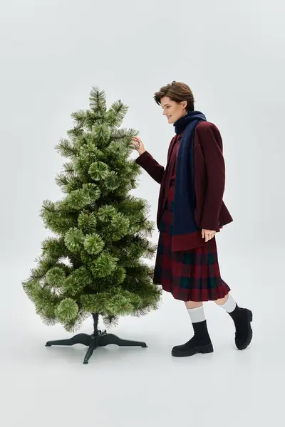 Eine stilvolle Frau in Winterkleidung arrangiert elegant Dekorationen am Weihnachtsbaum. — Stockfoto