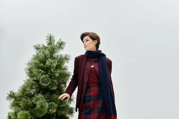 A beautiful woman dressed in stylish winter clothes poses thoughtfully next to a pine tree. — Stock Photo