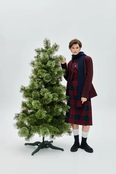 A beautiful woman dressed in cozy winter fashion stands beside a festive tree, exuding charm. — Stock Photo