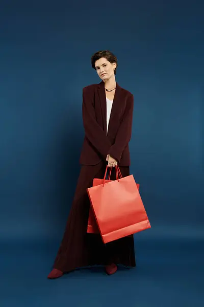 A stylish woman showcases her winter elegance, holding bright shopping bags against a bold backdrop. — Stock Photo