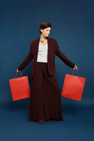 Una mujer elegante vestida con una acogedora moda de invierno muestra orgullosamente vibrantes bolsas de compras. - foto de stock