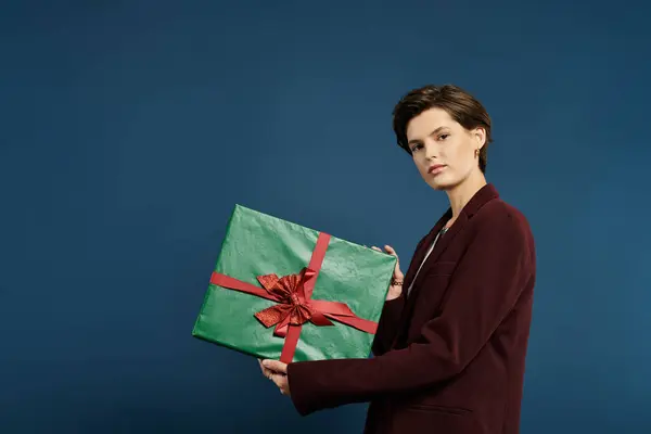 This elegant woman in winter attire presents a vibrant green gift, embodying festive joy and warmth. — Stock Photo
